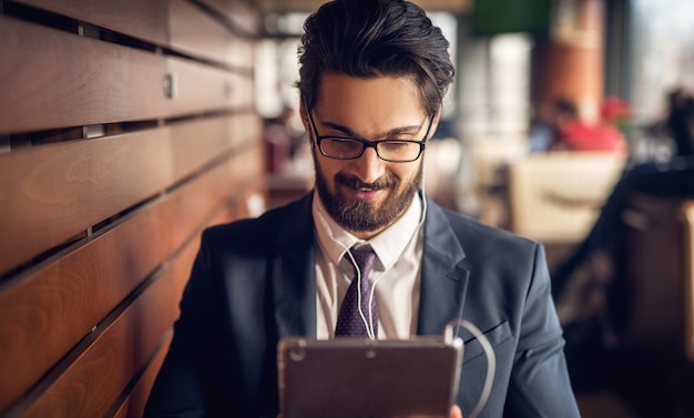 Junger hübscher moderner Geschäftsmann, der eine Pause am Kaffeehaus und unter Verwendung einer Tablette macht.