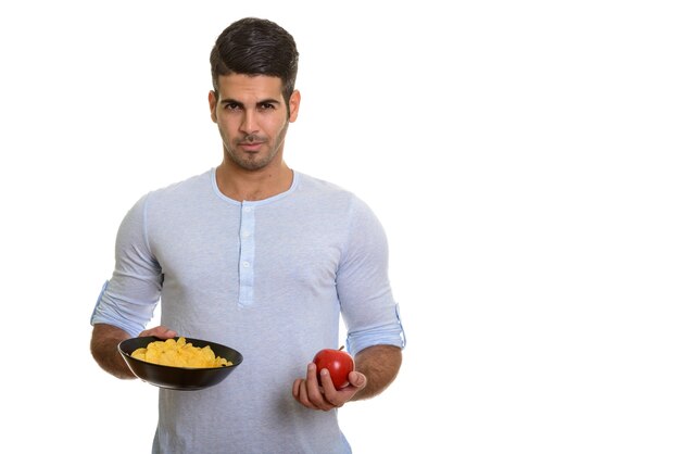 Junger hübscher persischer Mann, der Schüssel Kartoffelchips und roten Apfel hält