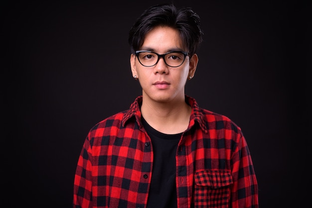 junger hübscher philippinischer Hipster-Mann mit Brille gegen schwarze Wand