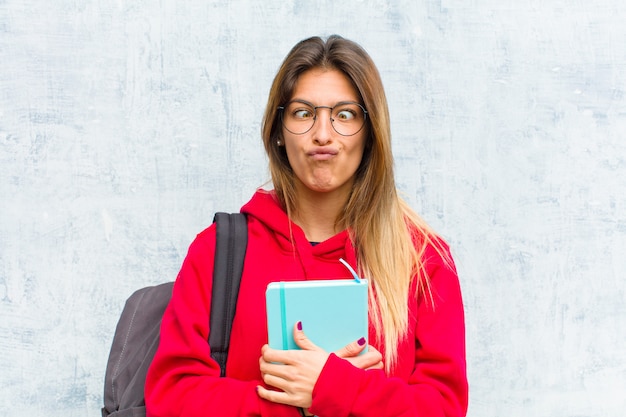 Junger hübscher Student, der doof und mit einem dummen cross-eyed Ausdruck lustig schaut, scherzt und herum täuscht