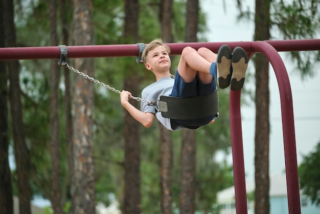 Junger, hübscher Teenager, der allein auf der Schaukel des Spielplatzes spielt, an einem sonnigen Tag im Sommerurlaub