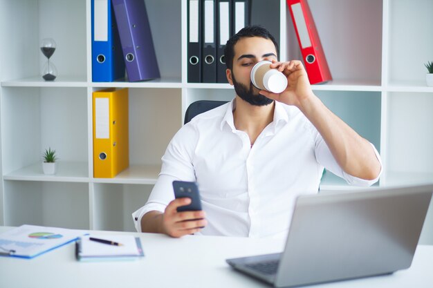 Junger hübscher Unternehmer, der am Schreibtisch sitzt und Laptop im Büro verwendet.