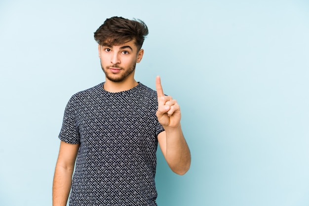 Junger Ian Mann auf einer blauen Wand, die Nummer eins mit Finger zeigt.