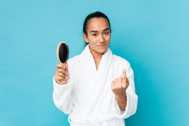 Junger Indianer der gemischten Rasse, der eine Haarbürste hält, die mit dem Finger auf Sie zeigt, als ob die Einladung näher kommt.