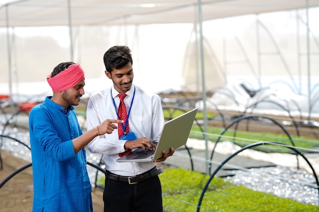 Junger indischer Agronom, der Landwirt einige Informationen im Laptop am Gewächshaus zeigt