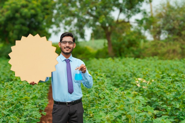 Junger indischer Agronomen, der Brett mit Kopienraum am Landwirtschaftsfeld zeigt.