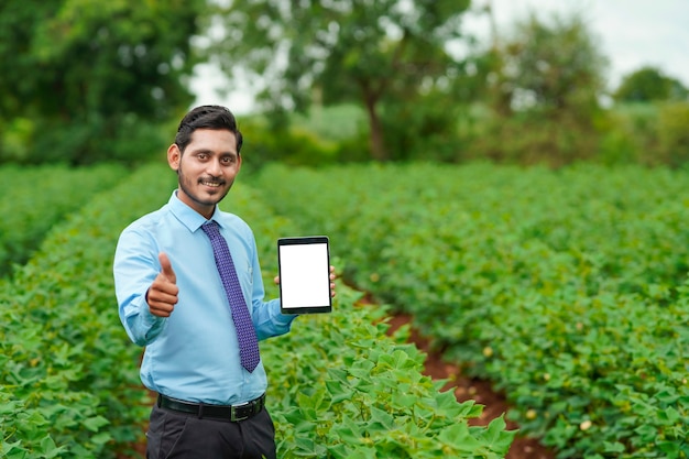 Junger indischer Agronomen oder Offizier, der Tablette am Landwirtschaftsfeld zeigt.