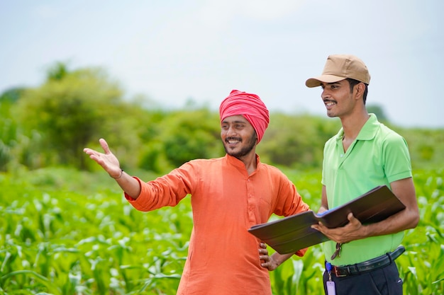Junger indischer Bankbeamter, der Papierkram mit Landwirten im Landwirtschaftsfeld erledigt.