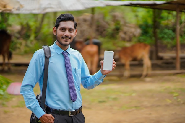 Junger indischer Bankbeamter oder Agronom, der Smartphone im Bauernhaus zeigt