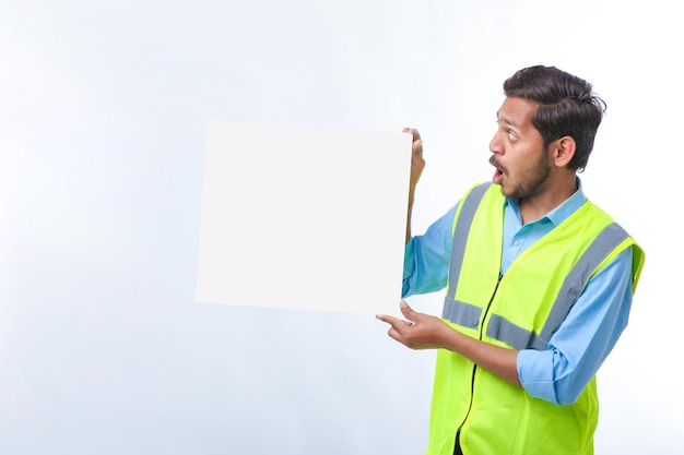Junger indischer Bauarbeiter, der leeres Plakatbrett auf weißem Hintergrund zeigt.