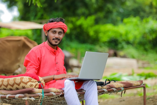 Junger indischer Bauer, der den Laptop benutzt