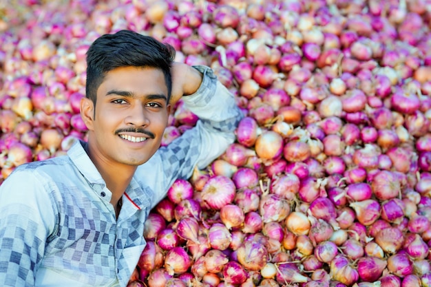 Junger indischer Bauer, der eine Zwiebel in der Hand auf dem Landwirtschaftsfeld hält