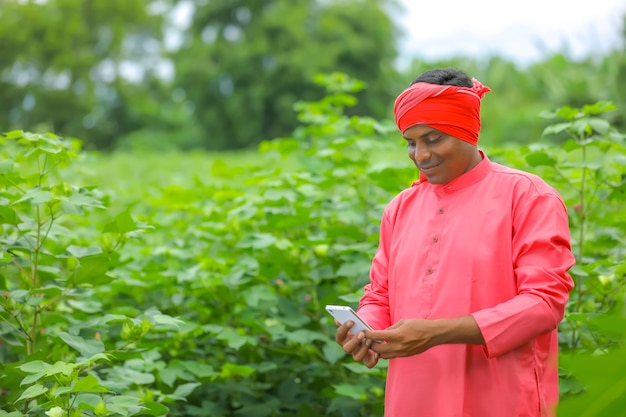 Junger indischer Bauer, der Handy am Landwirtschaftsfeld verwendet