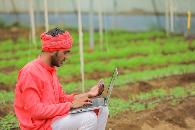 Junger indischer Bauer, der Laptop am Gewächshaus oder im Polyhaus verwendet
