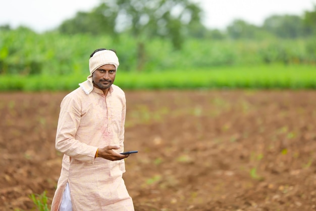 Junger indischer Bauer, der Smartphone am Landwirtschaftsfeld verwendet.