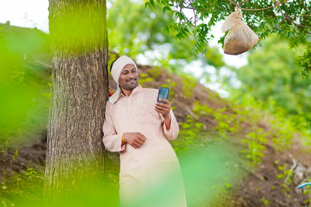 Junger indischer Bauer, der Smartphone am Landwirtschaftsfeld verwendet.