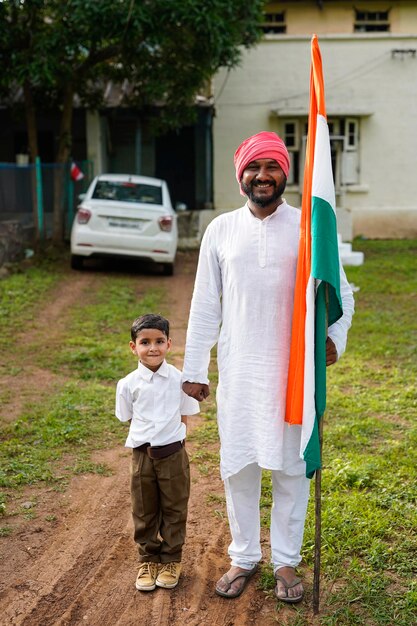 Foto junger indischer bauer und sein kind mit indischer flagge stehen vor dem haus