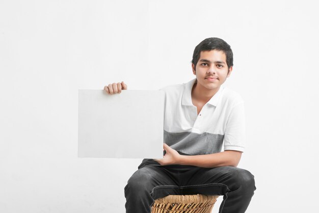 Junger indischer College-Student, der weiße Tafel auf weißer Wand zeigt