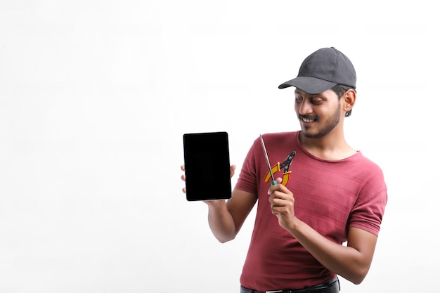 Junger indischer Elektriker, der Werkzeuge in der Hand hält und Smartphone zeigt.