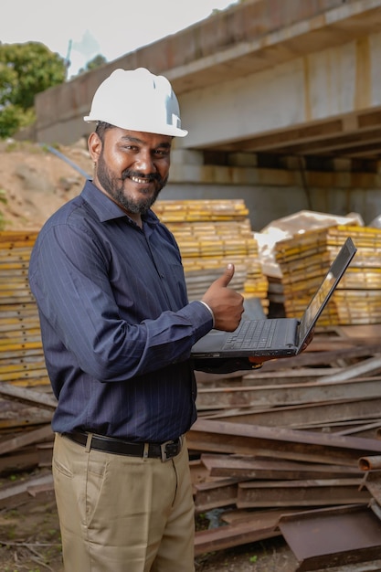 Junger indischer Ingenieur in Uniform und mit Laptop im Feld