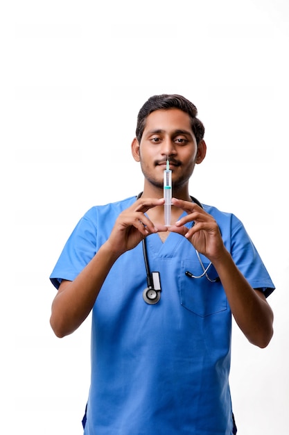 Junger indischer männlicher Doktor, der in der Hand geladene Spritze auf weißem Hintergrund hält.