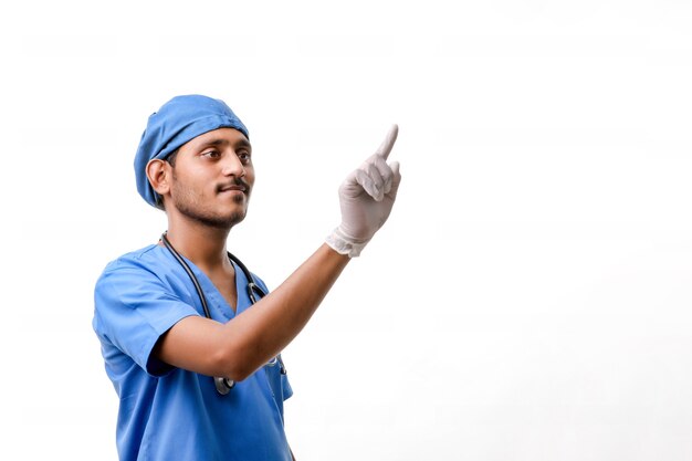 Junger indischer männlicher Doktor, der mit dem Finger über weißem Hintergrund zeigt.