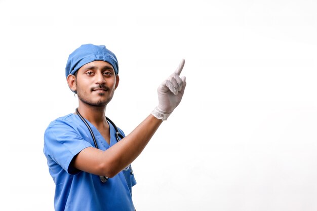 Junger indischer männlicher Doktor, der mit dem Finger über weißem Hintergrund zeigt.