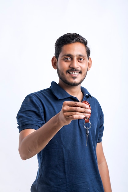 Junger indischer Mann, der in der Hand den Schlüssel über weißem Hintergrund hält.