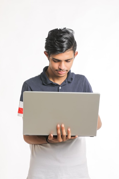 Junger indischer Mann, der Laptop über weißem Hintergrund verwendet.