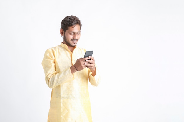 Junger indischer Mann in der Tradition tragen und Smartphone auf weißer Wand verwenden