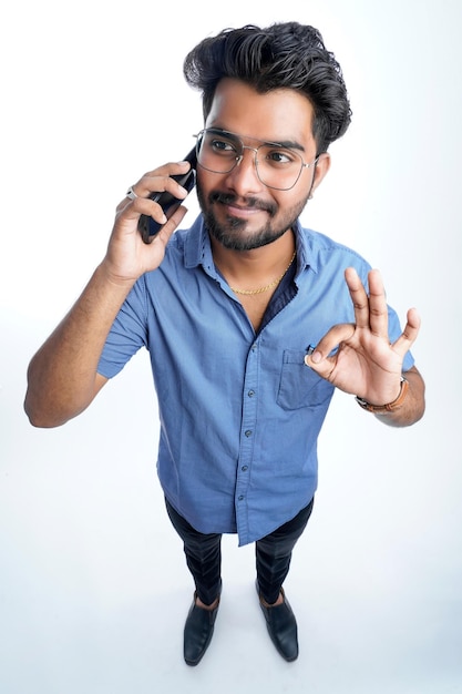 Junger indischer Mann mit Smartphone vor isoliertem weißem Hintergrund ernstes Gesicht, das über Frage oder Lösung nachdenkt sehr verwirrte Idee