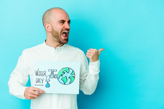 Junger kahlköpfiger Mann, der Weltwassertag lokalisiert auf blauen Wandpunkten mit Daumenfinger entfernt lacht und sorglos feiert