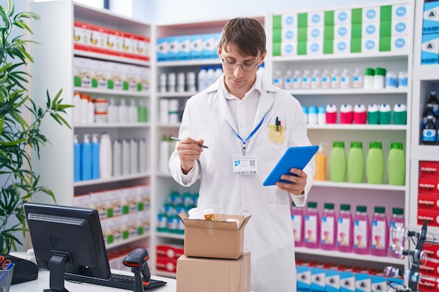 Junger kaukasischer Apotheker benutzt Touchpad und hält Tablettenfläschchen in der Apotheke