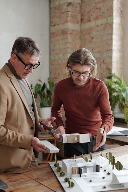 Junger kaukasischer Architekt mit Brille, der am Tisch steht und sein Projekt dem Chef präsentiert, der Materialproben hält