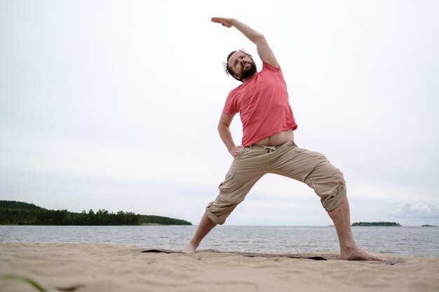 Junger kaukasischer bärtiger Mann praktiziert Yoga, er führt eine Übung im Stehen durch