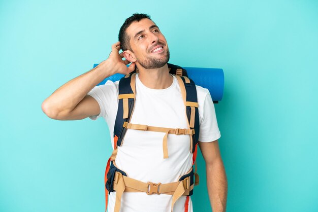 Foto junger kaukasischer bergsteigermann mit einem großen rucksack lokalisiert auf blauem hintergrund, der eine idee denkt