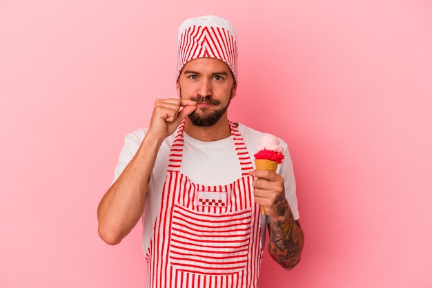 Junger kaukasischer Eismachermann mit Tätowierungen, die Eiscreme einzeln auf rosafarbenem Hintergrund mit Fingern auf Lippen halten, die ein Geheimnis halten.