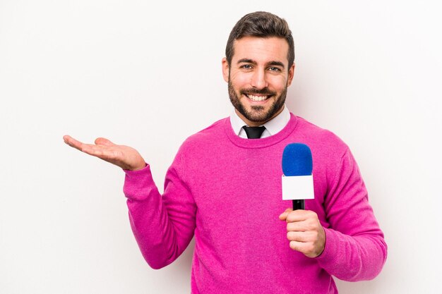 Junger kaukasischer Fernsehmoderator isoliert auf weißem Hintergrund, der einen Kopierraum auf einer Handfläche zeigt und eine andere Hand an der Taille hält