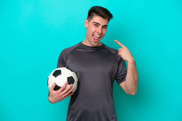 Junger kaukasischer fußballspielermann lokalisiert auf blauem hintergrund, der eine daumen hoch geste gibt
