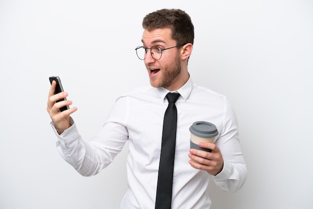 Junger kaukasischer geschäftsmann lokalisiert auf weißem hintergrund, der kaffee zum mitnehmen und ein handy hält