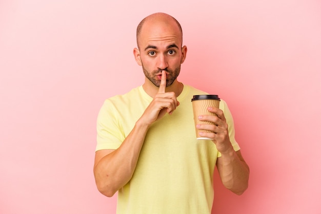 Junger kaukasischer glatzköpfiger Mann, der einen Kaffee zum Mitnehmen hält, der auf rosafarbenem Hintergrund isoliert ist, ein Geheimnis hält oder um Stille bittet.