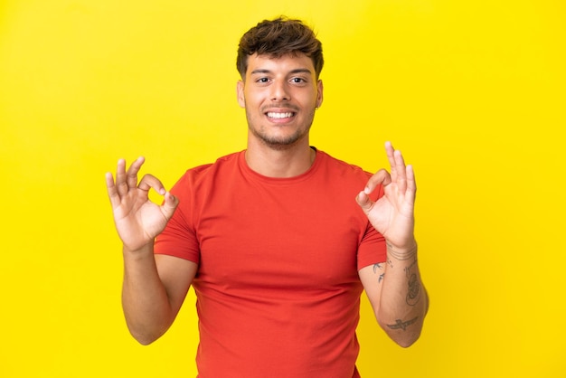 Junger kaukasischer gutaussehender Mann isoliert auf gelbem Hintergrund, der mit zwei Händen ein Ok-Zeichen zeigt