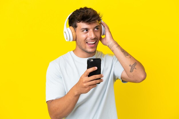 Junger kaukasischer gutaussehender Mann isoliert auf gelbem Hintergrund, der Musik mit einem Handy hört und singt