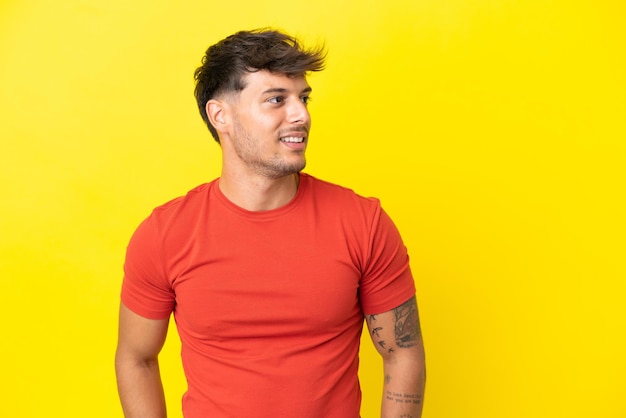 Junger kaukasischer gutaussehender Mann isoliert auf gelbem Hintergrund, der zur Seite schaut und lächelt