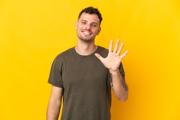 Junger kaukasischer gutaussehender Mann lokalisiert auf gelbem Zählen fünf mit den Fingern