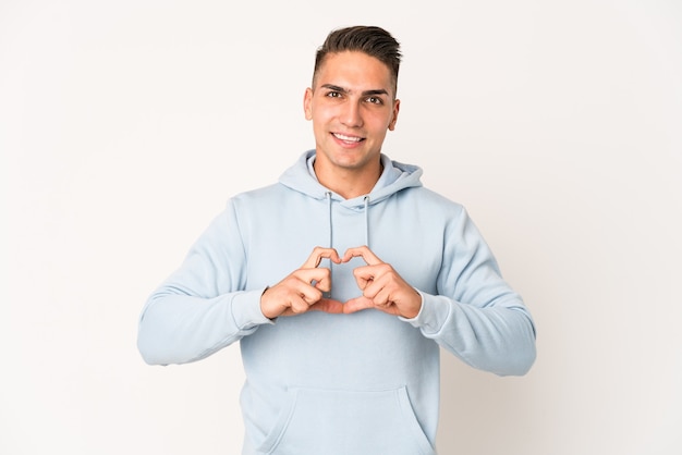 Junger kaukasischer gutaussehender Mann lokalisiert lächelnd und zeigt eine Herzform mit Händen.