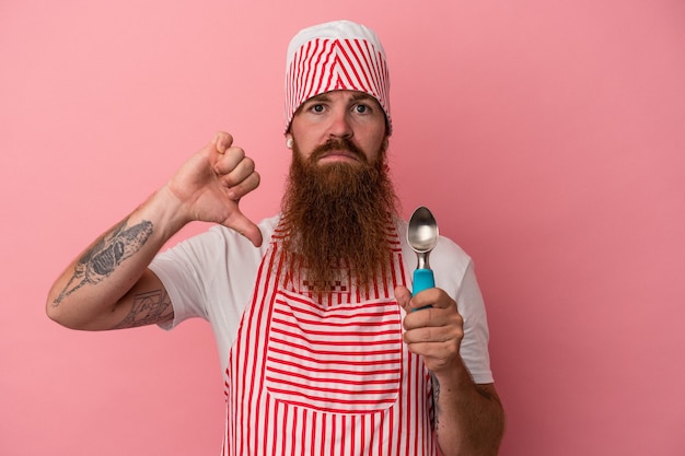Junger kaukasischer Ingwermann mit langem Bart, der eine Schaufel einzeln auf rosafarbenem Hintergrund hält, die eine Abneigungsgeste zeigt, Daumen nach unten. Meinungsverschiedenheit Konzept.