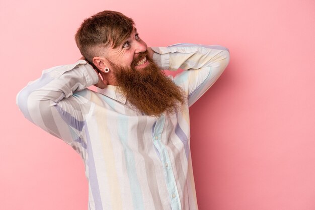 Junger kaukasischer Ingwermann mit langem Bart einzeln auf rosafarbenem Hintergrund, der sich selbstbewusst fühlt, mit den Händen hinter dem Kopf.