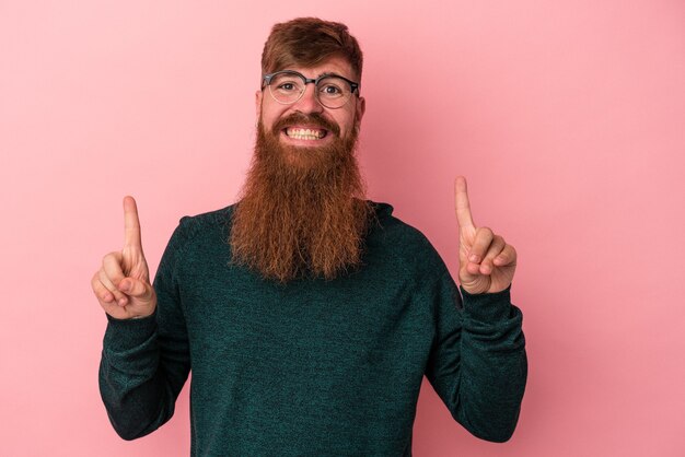 Foto junger kaukasischer ingwermann mit langem bart einzeln auf rosafarbenem hintergrund zeigt an, dass beide vorderfinger eine leerstelle zeigen.