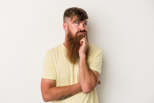 Junger kaukasischer Ingwermann mit langem Bart isoliert auf weißem Hintergrund, der nachdenkt, eine Strategie plant und über den Weg eines Unternehmens nachdenkt.